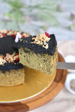 Load image into Gallery viewer, A slice of layered cake being lifted on a spatula, with a whole cake on a gold-rimmed wooden board in the background. The cake has a black sesame top layer, vegan fudge cake pea healthy diabetic friendly singapore